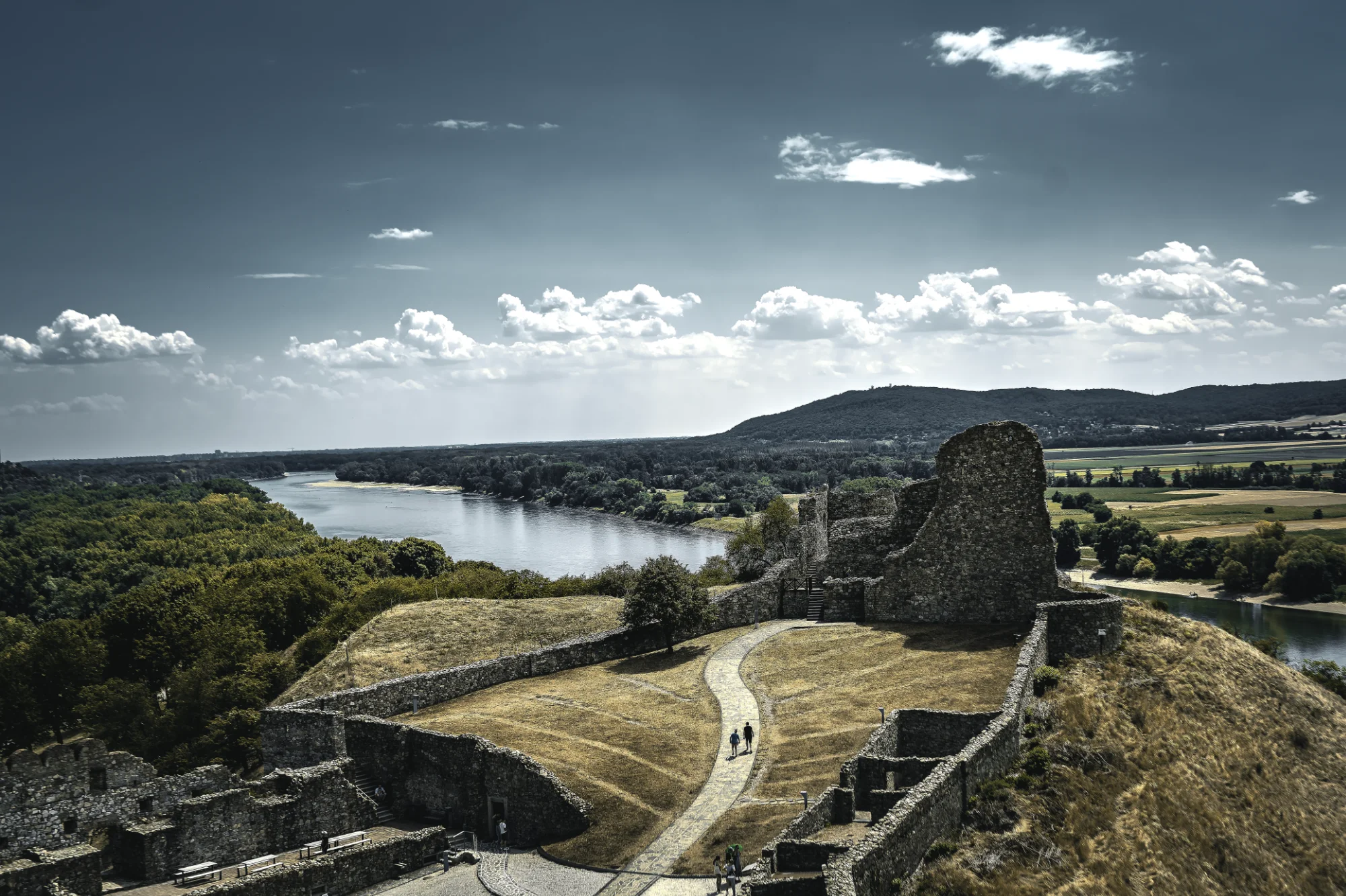 Devín Castle ruins overlooking the confluence of the Morava and Danube, with fields and forest under a clouded sky.