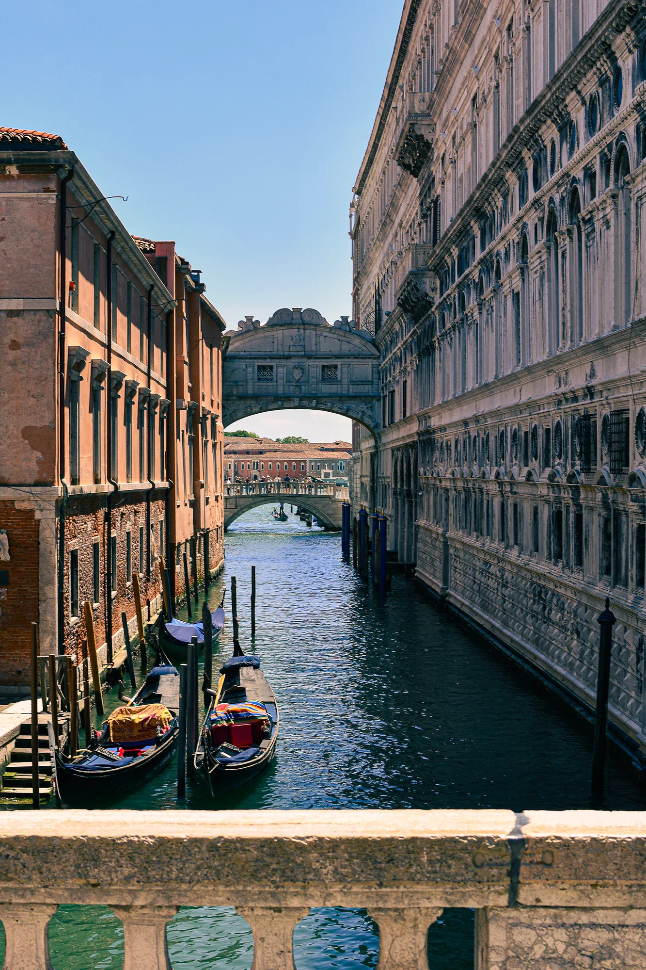 Vertical view along the Rio di Palazzo with gondolas below, the Bridge of Sighs overhead and another stone bridge in the distance.