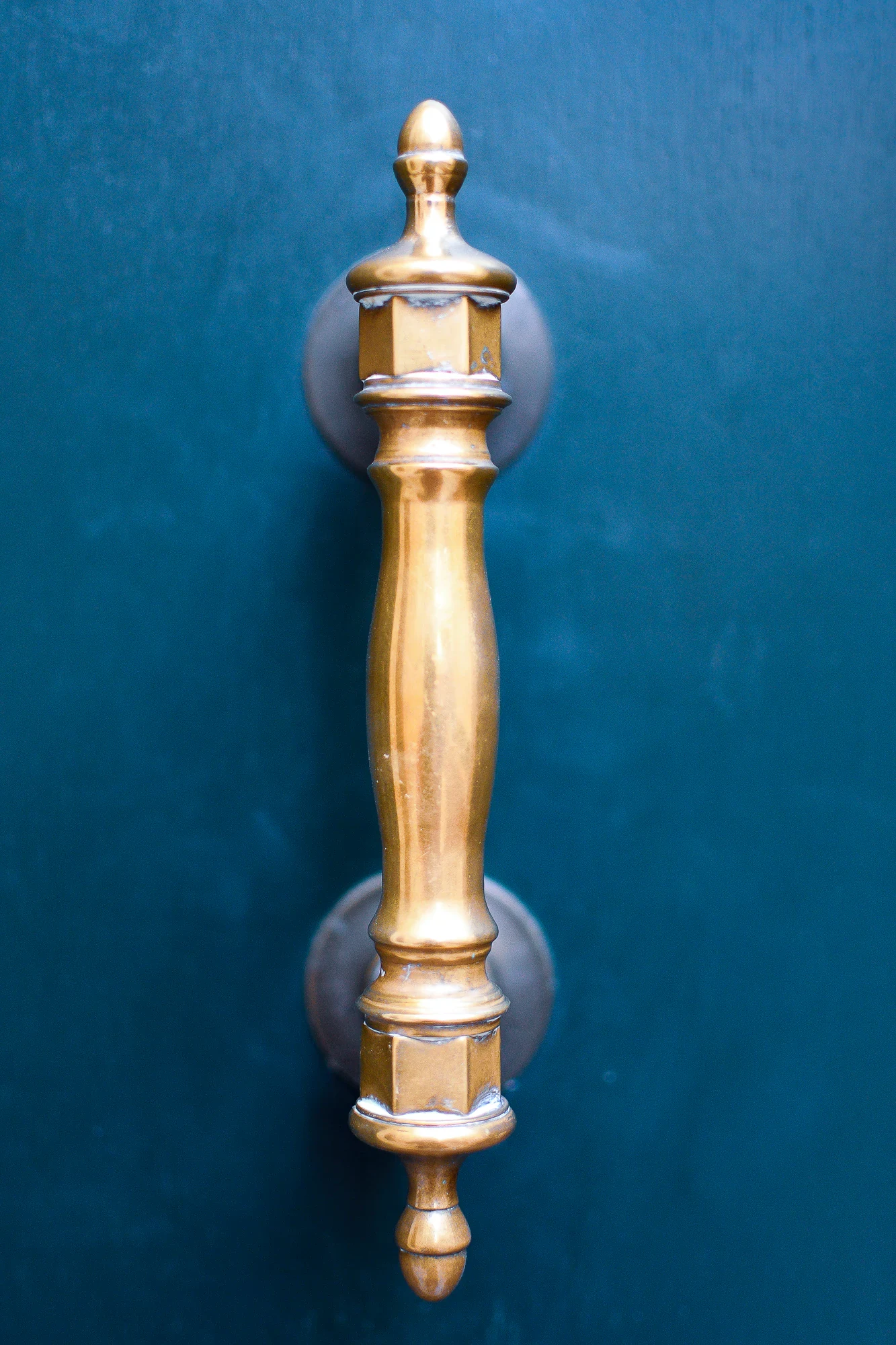 Polished brass door pull mounted vertically on a deep blue-green door in Venice.