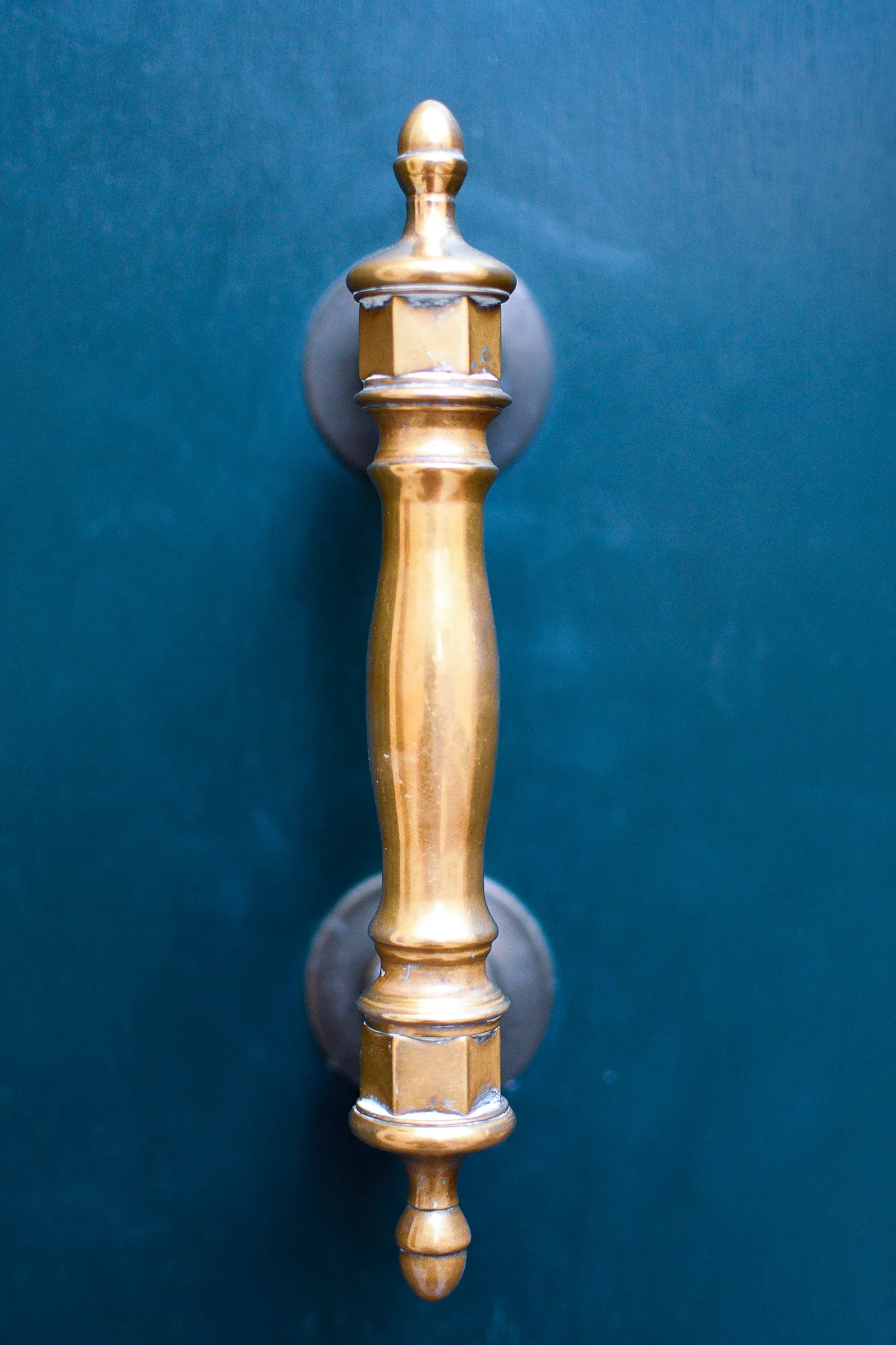 Polished brass door pull mounted vertically on a deep blue-green door in Venice.