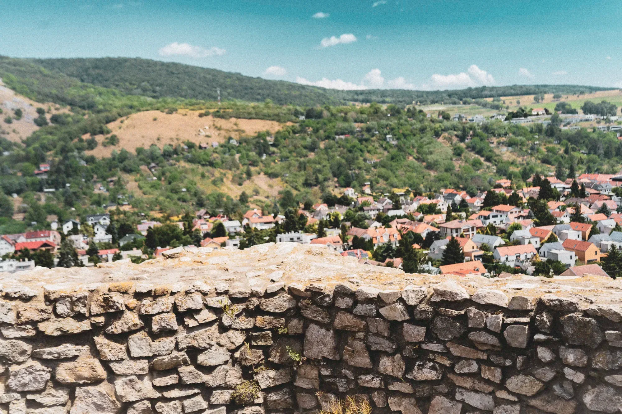 Rough stone parapet overlooking Devín village, red roofs and green fields beneath a blue sky.