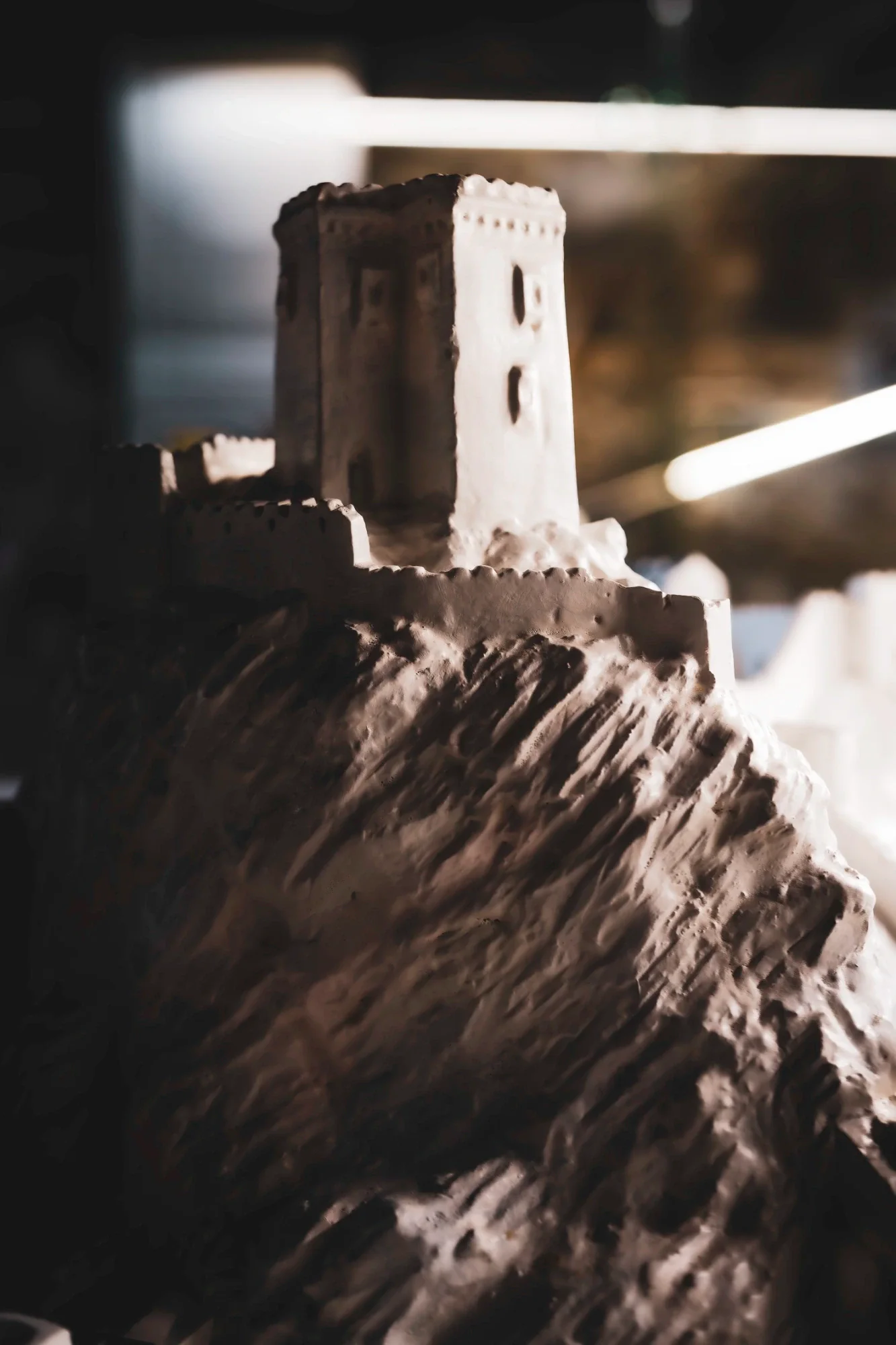 Small pale fortress model on textured terrain in strong side light against a dark background.